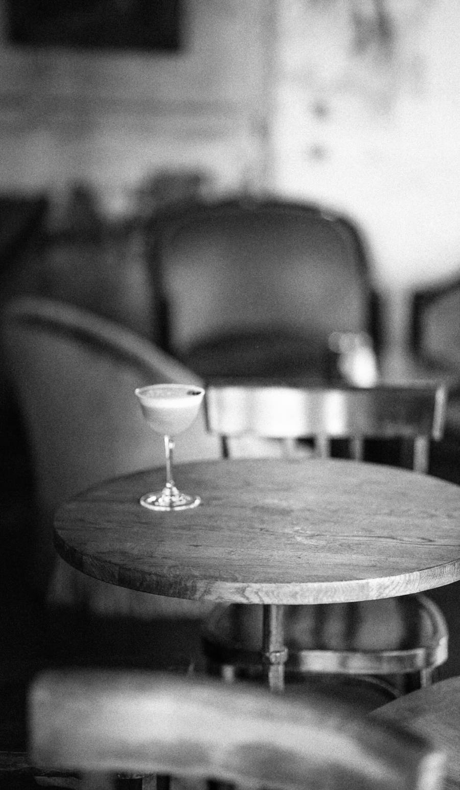 Une coupe de cocktail posée sur une table ronde en bois, dans un bar en lumière douce