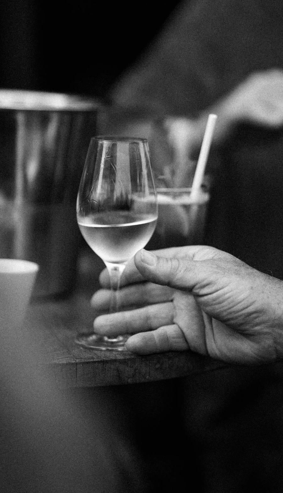 Une main tient un verre de vin blanc posé sur une table en bois