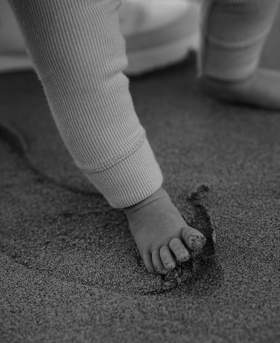 Le pied d'un tout-petit posé dans le sable, les orteils recouverts de grains