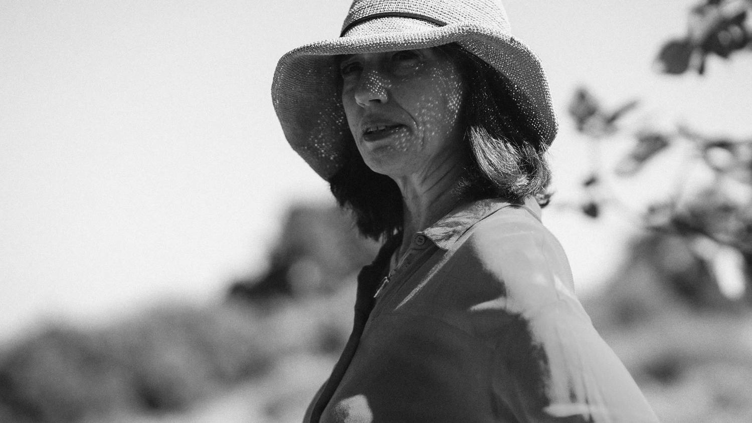 Portrait en noir et blanc d'une femme au chapeau de paille, le visage tacheté de lumière
